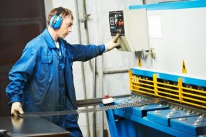 Fabrieksmedewerker aan het werk, in blauwe outfit met gehoorbescherming, drukkend op een knop