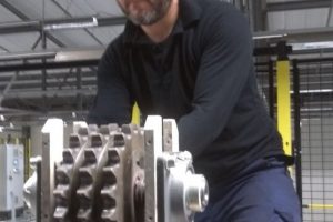 Close-up van een medewerker aan het werk in een fabriek, met een machine met tandwielen.
