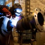 Lasser die een groot machineonderdeel aan het lassen is.